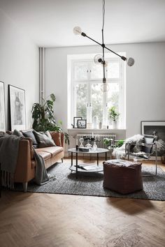 a living room with white walls and wooden floors, two couches, a coffee table, potted plants and pictures on the wall