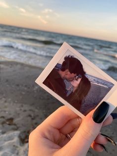 a person holding up a polaroid photo with the ocean in the background