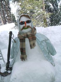 a snowman with sunglasses and a scarf is sitting in the snow next to an umbrella