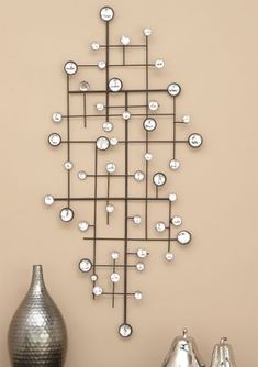 a metal wall sculpture with circles and dots on the top, in front of a vase