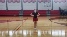 a woman wearing a face mask standing on a basketball court with her hands behind her back