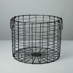 a black wire basket sitting on top of a white table next to a gray wall