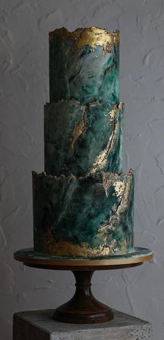 a three - tiered cake with green and gold marbled icing sits on a pedestal