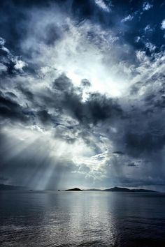 the sky is filled with clouds and sunbeams above water in front of an island