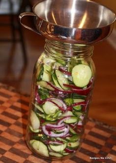 a glass jar filled with cucumbers and red onions on top of a checkered table