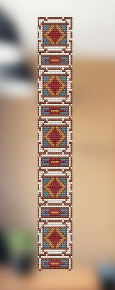 a cross stitch bookmark hanging on a wall in front of a blurry background