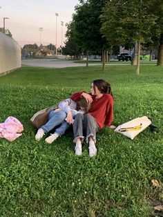 two people sitting in the grass with their arms around each other and one person laying on the ground