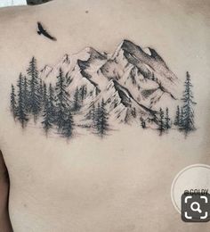 a man's back with a mountain and pine trees tattoo on his left side