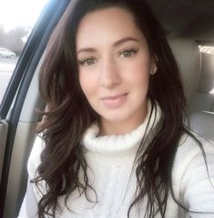 a woman sitting in the back seat of a car wearing a white turtle neck sweater