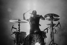 a woman playing drums on stage with her hands behind her head and the drum sticks in front of her