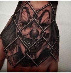 a person's hand with a tattoo of a clown behind a chain link fence