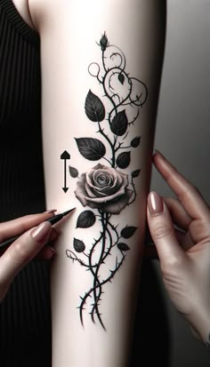 a woman with tattoos on her arm holding a pen and pointing at the rose tattoo