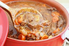 a spoon full of stew with carrots and meat in it on top of a red pot