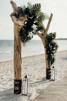 an outdoor ceremony setup on the beach with lanterns and greenery in front of it