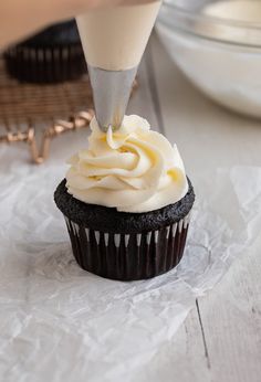 a cupcake being frosted with white icing on top of a piece of paper