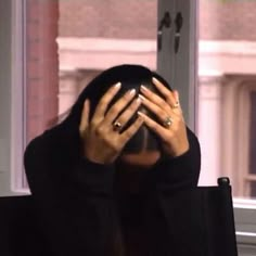 a woman covering her face with both hands while sitting in front of a large window