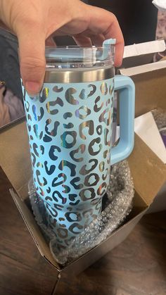 a person holding onto a blue and silver coffee cup in a box with its lid open