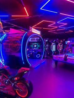 a room filled with arcade machines and neon lights on the ceiling, as well as a motorcycle parked in front of it