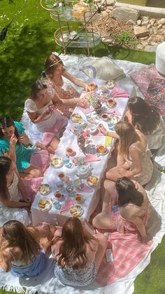 a group of women sitting at a picnic table eating cake and drinking tea outside in the sun