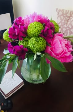 a vase filled with pink and green flowers on top of a wooden table next to a book