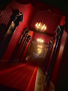 a hallway with red walls and chandeliers on the ceiling is lit by candles