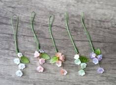 four different colored flowers are hanging from green cords on a wooden surface with leaves and beads