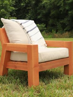 a wooden chair sitting in the grass with pillows on it's back and side