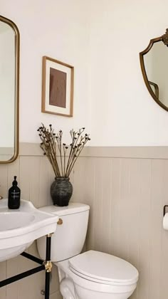 a white toilet sitting next to a sink in a bathroom under a large framed mirror