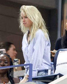 a blonde woman sitting in the stands at a tennis match with other people watching her