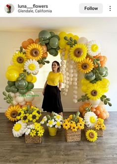 a woman standing in front of a bunch of fake sunflowers and flowers on display