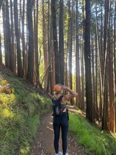 a woman standing on a trail in the woods looking up at trees and holding an orange object over her head