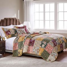 a bedroom with a large bed covered in colorful quilted bedspread and pillows