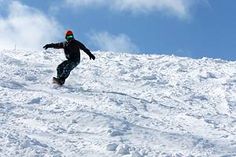 a man riding a snowboard down the side of a snow covered slope on a sunny day