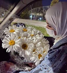 a woman wearing a white head scarf sitting in a car with daisies