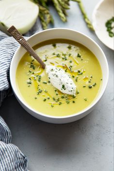 a white bowl filled with soup next to asparagus and cheese on a table