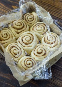 several cinnamon rolls wrapped in plastic on a wooden table