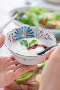 a person is holding a bowl with yogurt in it while another hand holds a spoon