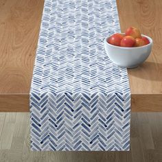 a bowl of fruit sitting on top of a table next to a blue and white runner