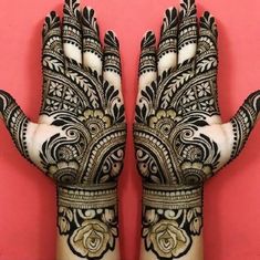 two hands that are decorated with henna designs on pink wall behind the hand is an intricate design