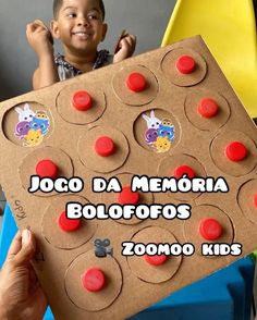 a young boy holding up a cardboard board with buttons on it and the words jogo da memoia bolofoos zooo kids