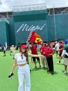 a woman holding a red and yellow flag in front of a large green field with people standing around