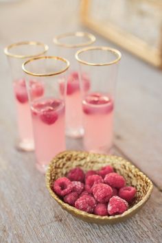 raspberries in glasses with gold rims on a wooden table next to pink drinks