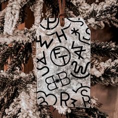 a christmas ornament hanging from a tree with writing on it and snow covered branches