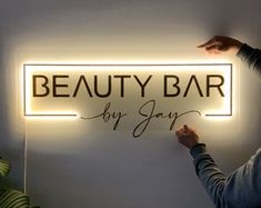 a woman holding up a sign that says beauty bar by jayy on the wall