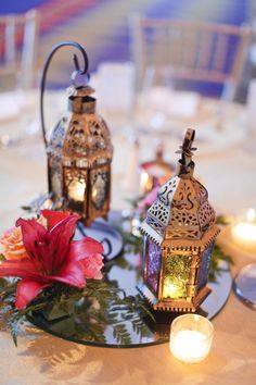 two small lanterns sitting on top of a table next to flowers and candlelight holders