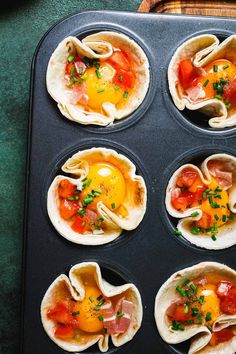 an open muffin tin filled with eggs, ham and tomatoes on top of tortilla shells