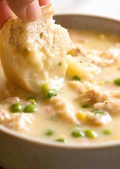 a hand dipping a piece of bread into a bowl of chicken pot pie soup with peas