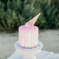 a pink and white cake with an ice cream cone on top is sitting on a table