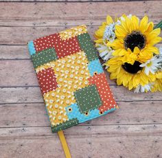 a yellow sunflower sitting on top of a wooden table next to a notebook cover