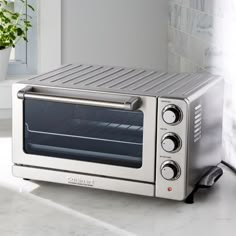 a silver toaster oven sitting on top of a counter next to a potted plant